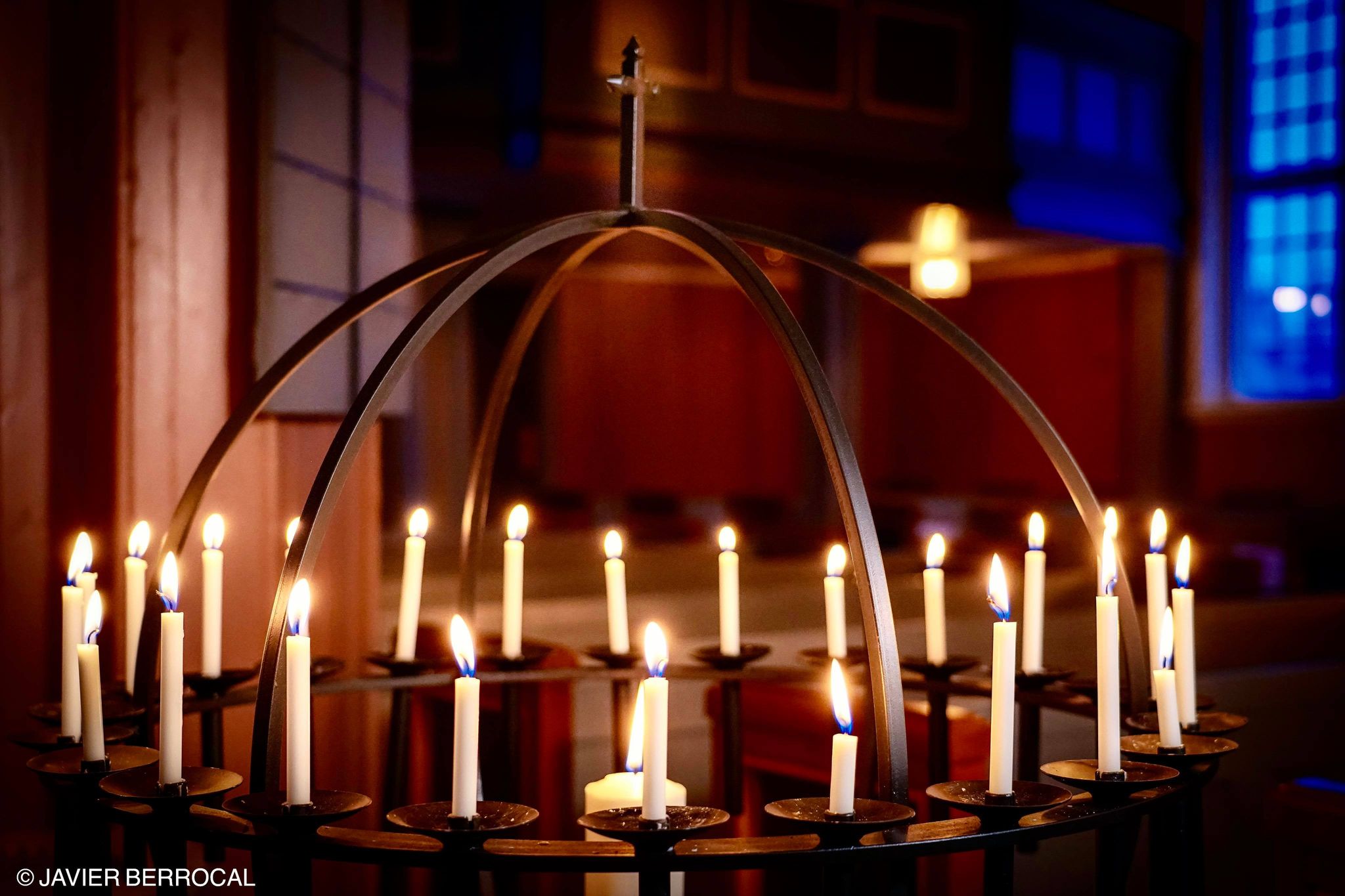 Nærbilde av en lysglobe, fullsatt med små lys, mot et rødlig kirkrom.