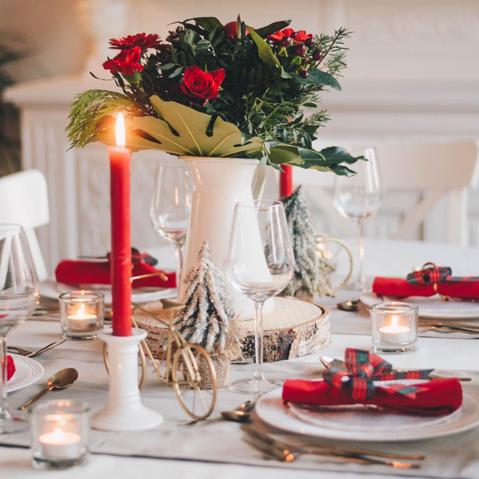 Festpyntet bord med julepynt og høye glass, pynt i rødt og grønt.