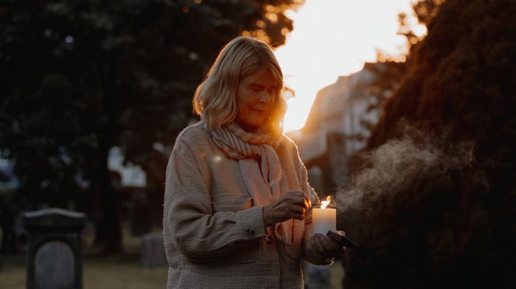 Eldre dame tenner lys ute på en gravplass